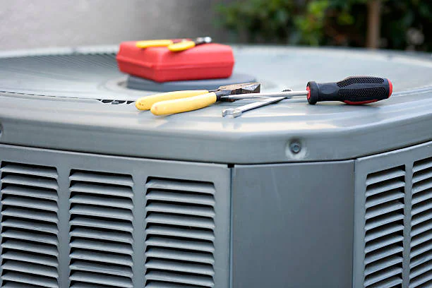 Screwdrivers, pliers, and a red toolbox resting on top of an outdoor air conditioning condenser unit ready for repair.