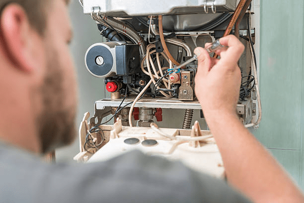 Close-up of a technician's hand adjusting internal components and tubing inside an open residential boiler unit.