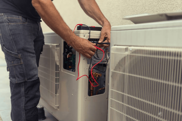 Close-up of a technician's hands working on the internal wiring and components of an outdoor air conditioning condenser unit.