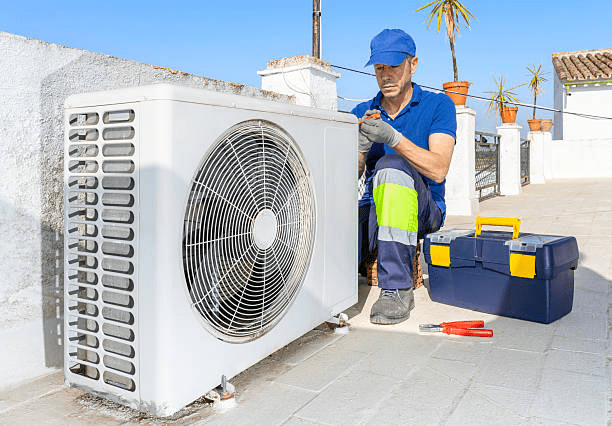 HVAC technician kneeling beside a rooftop air conditioning condenser unit with a toolbox and pliers nearby, set against a sunny rooftop terrace.